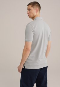 Tricou polo din bumbac gri văzut din spate, având un guler clasic și mâneci scurte, cu fante laterale și cusături curate.