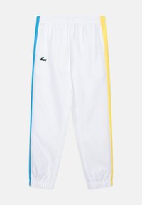 Pantaloni da pista bianchi con strisce laterali blu e gialle, vita elastica e un piccolo logo verde Lacoste sulla gamba sinistra.