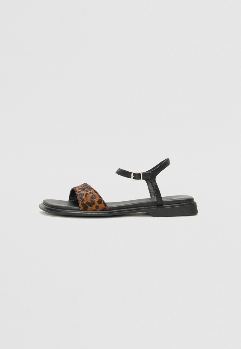 Sandale en cuir noir à imprimé léopard avec une bride autour de la cheville, une semelle plate, un bout ouvert et un design minimaliste.