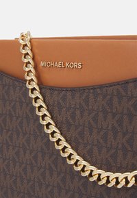 Brun mønstret håndtaske med en guldkæde-rem, beige læderdetalje og indgraveret "MICHAEL KORS" logo øverst.
