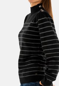 Zwarte gestreepte trui met hoge kraag, voorzien van zilveren horizontale strepen, drie decoratieve knopen op de schouder en geribbelde manchetten.