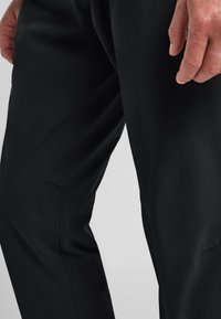 Zwarte broek van soepel, lichtgewicht stof. Strak ontwerp met een taps toelopende vorm en subtiele naden. Geen zichtbare patronen of hardware.