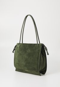 Borsa a tracolla verde in suede con doppio manico, caratterizzata da un design pieghevole e un accento in oro con il logo. Texture morbida e linee semplici.