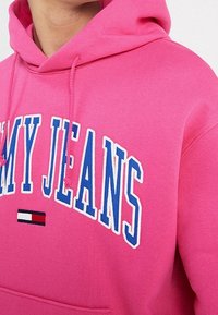 Sudadera rosa de algodón, con un gráfico frontal "MIS VAQUEROS" en blanco y azul, con un pequeño logotipo en rojo y blanco.