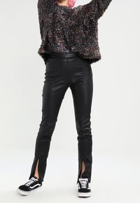 Pantalones de piel sintética negra con aberturas laterales, combinados con un suéter texturizado multicolor y zapatillas negras. Acabado suave y diseño ajustado.