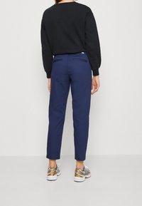 Sweat-shirt noir et pantalons navy avec poches arrière, présentant un design fuselé. Assortis à des baskets arborant une combinaison de couleurs argent et orange.