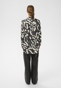 Pikad varrukad särgil must-valge abstraktse mustriga, valmistatud kerge kangaga. Sobitatud kõrge vöökohaga, laia säärega kunstnahast pükstega.