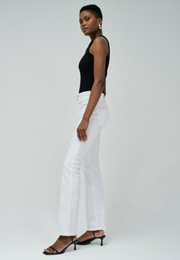 Top noir sans manches, jeans bootcut blancs et sandales à talons noires. Tissu lisse, design ajusté et boutons proéminents à la taille.