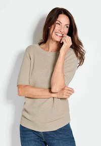 Lichtbeige gebreide trui met een wijde halslijn en korte mouwen, gecombineerd met blauwe jeans. Zachte textuur en geribbelde accenten op de mouwen en de zoom.