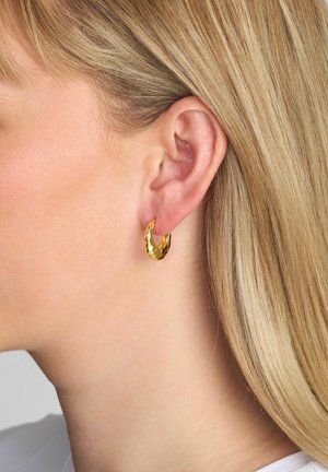 Cercei cercel din aur cu un design ondulat și texturat. Cerceii sunt de mărime medie, având o suprafață reflectorizantă care prinde lumina.