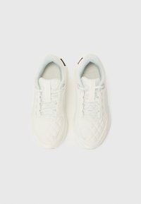 Sneakers bianchi con una texture trapuntata, caratterizzati da un design con lacci, colletto imbottito morbido e un sottile marchio sul lato.