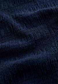 Tissu bleu marine texturé avec une surface ondulée, présentant des motifs alternés en relief et en creux, doux au toucher et léger.