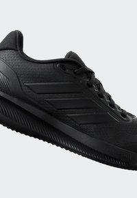 Des chaussures de sport noires avec un dessus texturé, un design à trois bandes sur le côté, et une semelle en caoutchouc avec un motif strié pour une meilleure adhérence.
