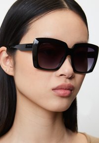 Zwarte oversized zonnebril met een gedurfde geometrische montuur. Verlooplenzen en een glanzende afwerking benadrukken eigentijdse designelementen.