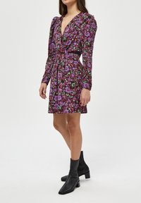 Blumenkleid mit tiefem V-Ausschnitt, langen Ärmeln und tailliertem Bund. Hergestellt aus leichtem Stoff in Lila-, Rosa- und Grüntönen.
