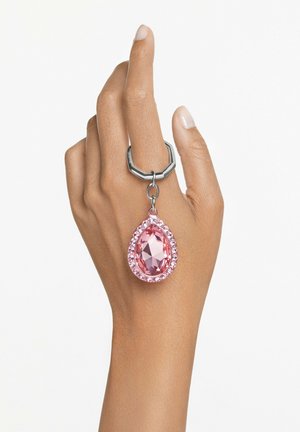 Mano dalla pelle marrone chiaro con anello d'argento che tiene un grande ciondolo a forma di goccia di pietra preziosa rosa.