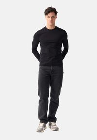 Czarna, długosleeve'owa koszula z okrągłym dekoltem, dopasowany krój; w połączeniu z ciemnymi dżinsami i szarymi sneakersami z teksturowanym wzorem.