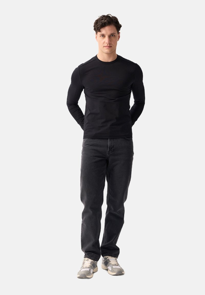 Czarna, długosleeve'owa koszula z okrągłym dekoltem, dopasowany krój; w połączeniu z ciemnymi dżinsami i szarymi sneakersami z teksturowanym wzorem.