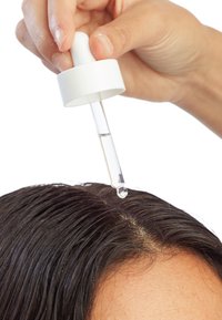 Flacon compte-gouttes avec un bouchon blanc distribuant un liquide clair sur des cheveux raides et foncés, mettant en valeur une texture propre et brillante.
