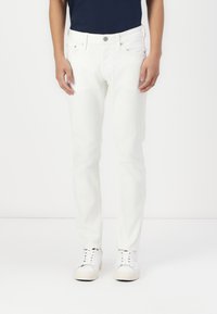 White denim jeans with a slim fit, five-pocket design, front button closure, and plain texture, paired with white sneakers.