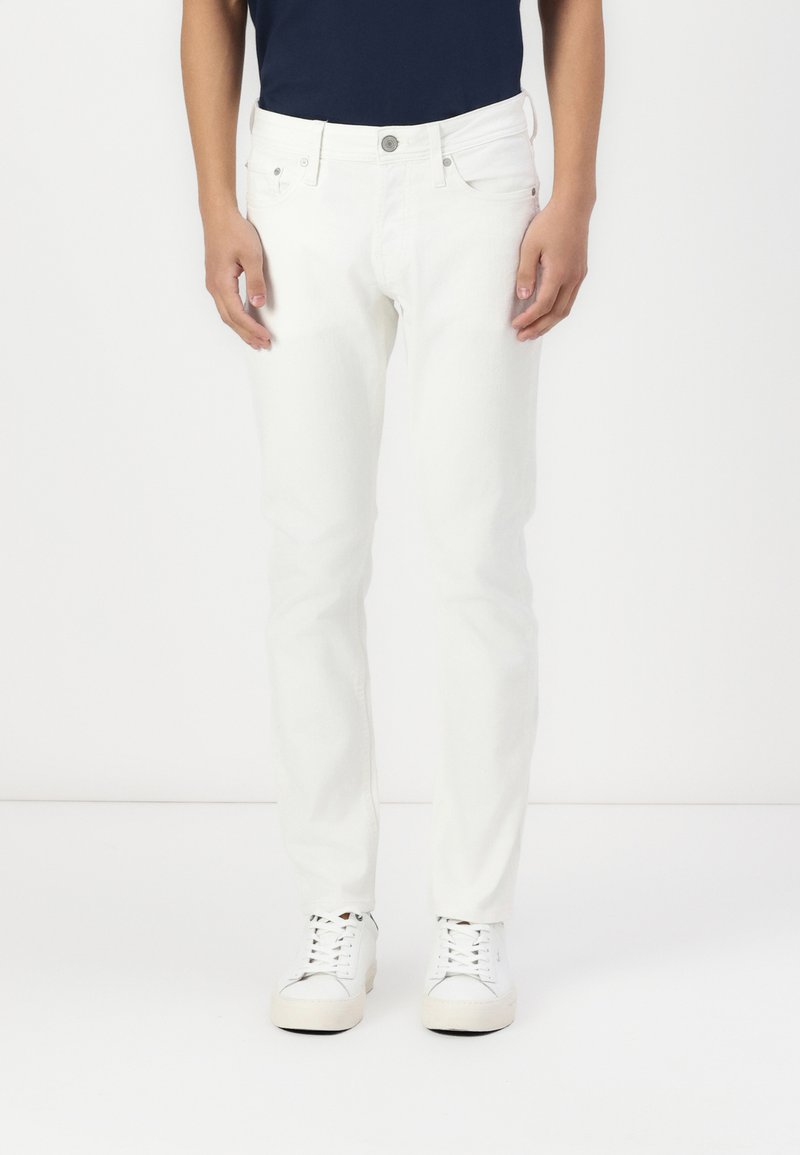 White denim jeans with a slim fit, five-pocket design, front button closure, and plain texture, paired with white sneakers.
