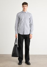 Lyseblå skjorte med knapper og små hvite mønstre, sammen med svarte bukser og en svart tote bag. Antrekket har en avslappet passform og en klassisk krage.