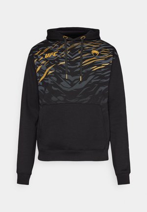 Black hoodie with a front pocket, featuring a yellow and gray tiger stripe pattern, drawstring hood, and gold accent details on the neckline.