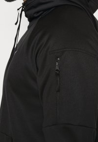 Svart zip-up hoodie med texturerad tyg, en framficka och en ficka med dragkedja på ärmen, prydd med svarta detaljer.