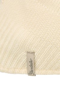 Cream-colored knitted fabric with ribbed texture and a small beige tag featuring black cursive text.