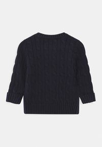 Granatowy sweter z dzianiny z teksturowanym wzorem w warkocze, ze ściągaczami na mankietach i dekolcie. Posiada długie rękawy i okrągły kołnierz. Widok z tyłu.