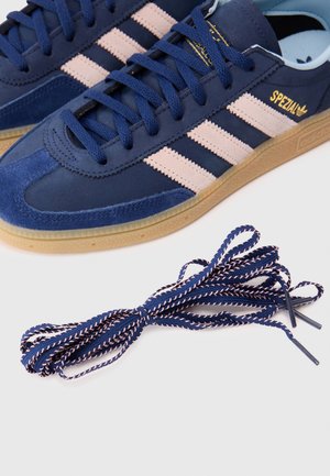 Laivastonsiniset Adidas Spezial -lenkkarit beigen värisillä raidoilla ja kumipohjilla, yhdessä parin sopivien tummansinisten ja beigen väristen kengännauhojen kanssa.
