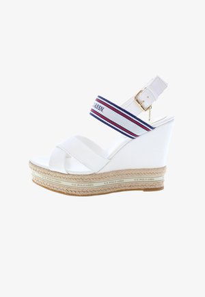 Bílé klínové sandály s křížovým páskovým designem, textilní kotníkový pásek s červenými a modrými pruhy a pletené detaily připomínající jutovou podešev.