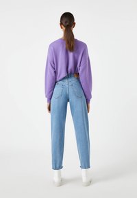 Fioletowy, oversize'owy sweter z opuszczonymi ramionami, w połączeniu z jasnoniebieskimi, wysokimi dżinsami. Białe, masywne buty na platformie dopełniają strój.