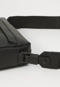 Black leather shoulder bag with textured finish, featuring a sleek design, adjustable strap, and prominent hardware detailing on the buckle.