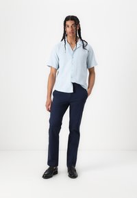 Chemise boutonnée à manches courtes bleu clair associée à un pantalon bleu foncé et des mocassins noirs. Tissu texturé, coupe décontractée, design simple.