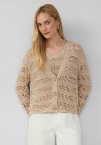 Beige Strickjacke mit offener Maschenstruktur, gestreiftem Muster und drei Knöpfen vorne. Leichtes Material, kombiniert mit einem einfachen Oberteil.