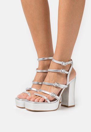 Sandale argintii cu toc înalt, dotate cu o platformă masivă, curele multiple cu catarame, design cu degetele expuse și finisaj metalic neted.