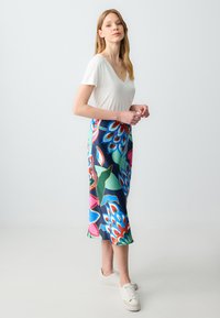 Witte V-hals t-shirt gecombineerd met een kleurrijke bloemenpatronen zoomrok in tinten blauw, groen, roze en rood met een gladde textuur.