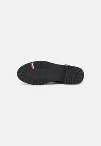 Suela de zapato de goma negra con profundos surcos para tracción, un detalle de franjas blanca y roja, y acentos de patrón hexagonal.