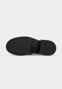 Semelle d'une chaussure habillée noire montrant un cuir lisse cousu avec un bout arrondi et un talon noir solide sur un fond clair.