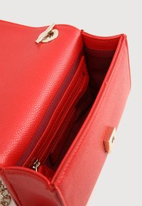 Interno di una borsa a tracolla in pelle rossa testurizzata con scomparto con zip e slot per carte, caratterizzata da una chiusura e dettagli in catena in tono oro.