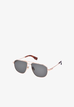 Lunettes de soleil aviateur à monture métallique avec verres teintés foncés et branches marron sur fond blanc.