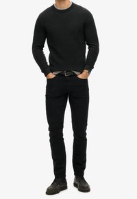 Suéter de punto gris oscuro con un escote redondo, combinado con jeans negros ajustados y zapatos de cuero negros. Incluye un reloj y un cinturón visibles.