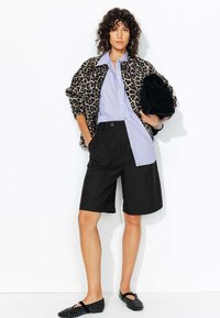 Veste en imprimé léopard, chemise rayée bleu clair et blanche, shorts plissés noirs, pochette noire et ballerines noires à motifs.