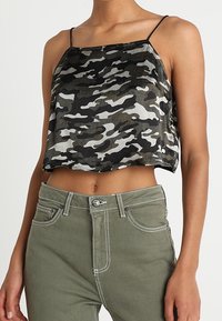 Top a maniche corte mimetico in nero e verde, con spalline sottili e una silhouette ampia. Abbinato a jeans a vita alta verde oliva.