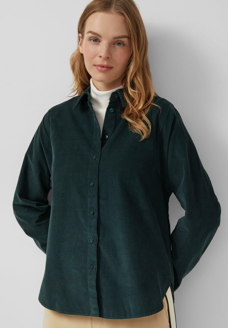 Chemise boutonnée vert foncé en tissu doux, avec un col classique, des manches longues et une coupe décontractée. Détails de bouton simples et texture lisse.