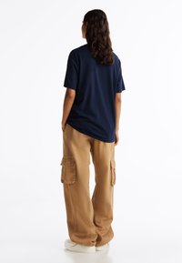 Marineblå t-skjorte med korte ermer kombinert med beige cargo-bukser. Buksene har store sidelommer og et tekstlogo på baklommen. Strukturert stoff.