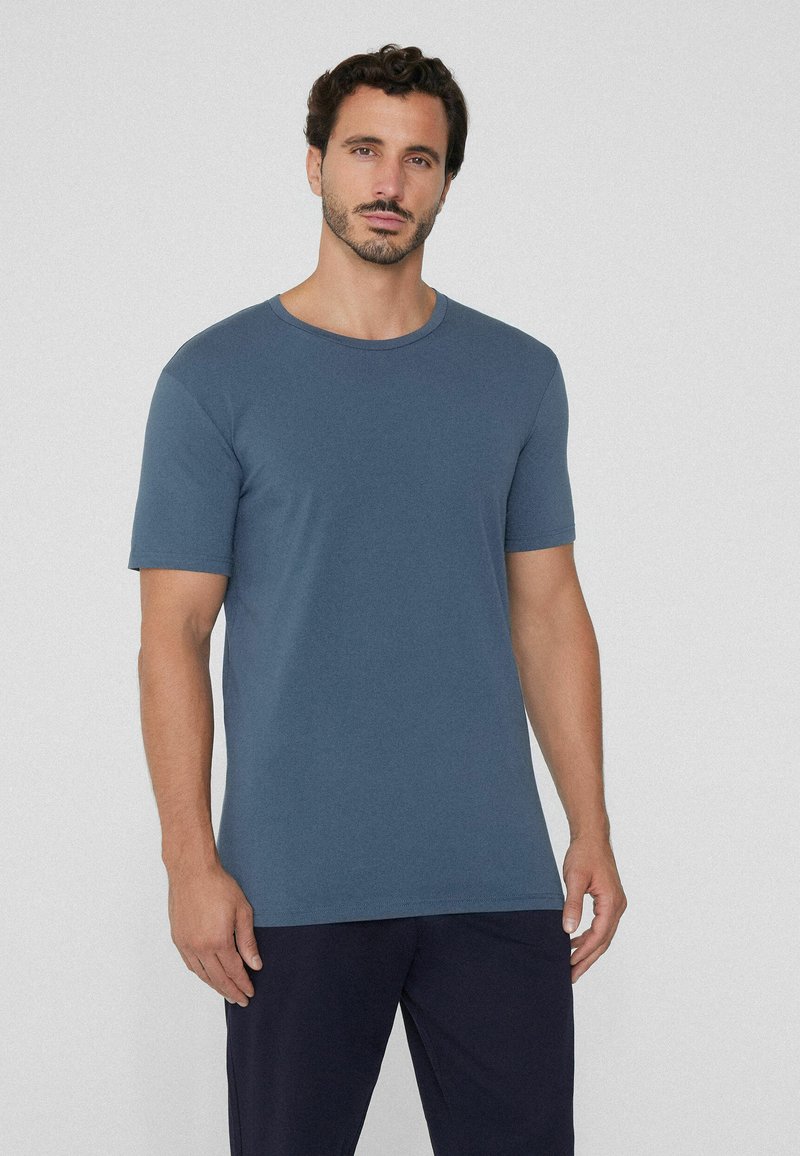 Camiseta de manga corta azul hecha de algodón, con un cuello redondo y una textura suave. Combinada con pantalones oscuros, diseño minimalista.