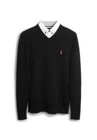 Pull noir en maille avec un col en V, manches longues et petit logo homard orange sur le côté gauche de la poitrine. Superposé à une chemise blanche à col.
