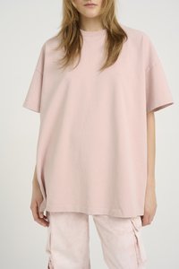 Rosa oversized t-skjorte, rund hals, korte ermer, mykt bomullsmateriale, har subtil logo detaljer på brystet. Kombinert med lyse rosa cargo-bukser.